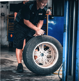 A man wearing a shirt that says alter car automotive works on a tire | All-Star Automotive