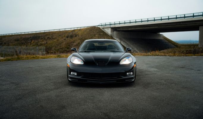 A black sports car is parked in a parking lot under a bridge.