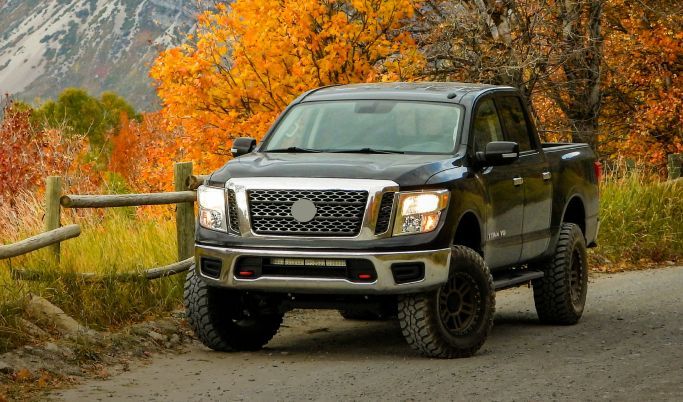 A black truck is parked on the side of a road next to a fence.