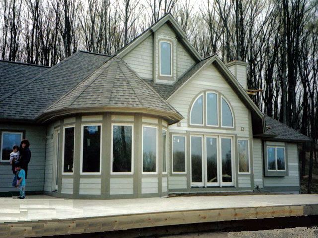 House with a curved window section, tall windows, and a person holding a child on a patio.