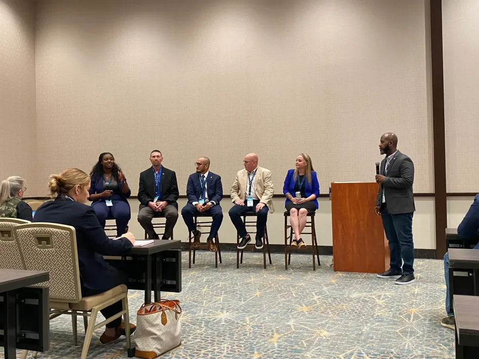 A group of people are sitting in chairs in a room while a man stands at a podium giving a presentation.
