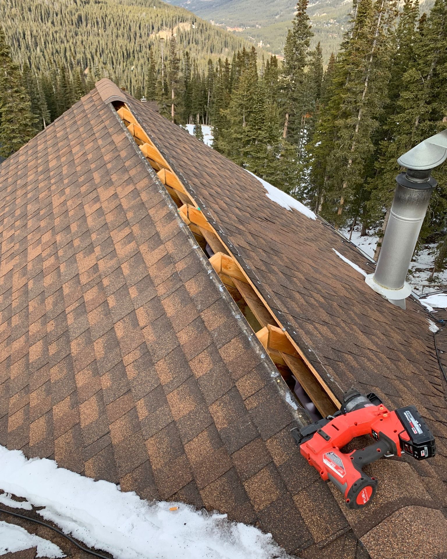 Workers on a scaffold and lift replace shingles on a large, steep brown roof under a blue, cloudy sky.