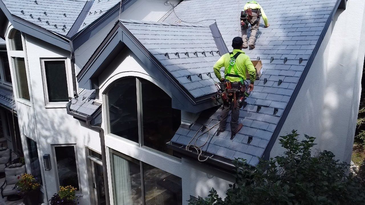 Two workers in safety gear repairing a gray roof on a house