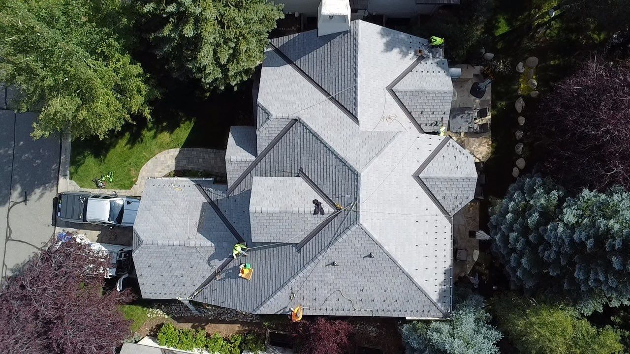 Aerial view of a gray-roofed house surrounded by trees, with a driveway and parked vehicle.