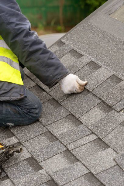 Professional roofer in protective gear installing asphalt roofing tiles on a house under construction