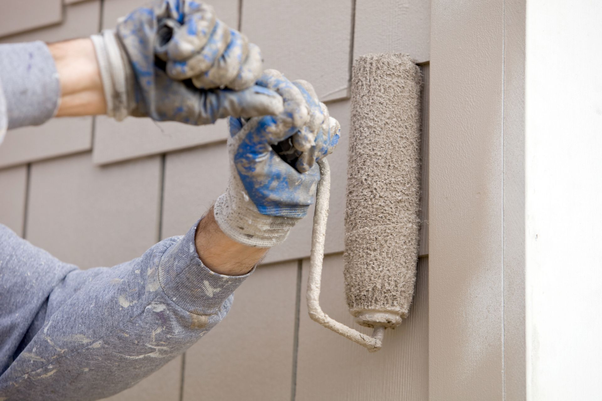 House painter paints the exterior shingles of a house with a paint roller.