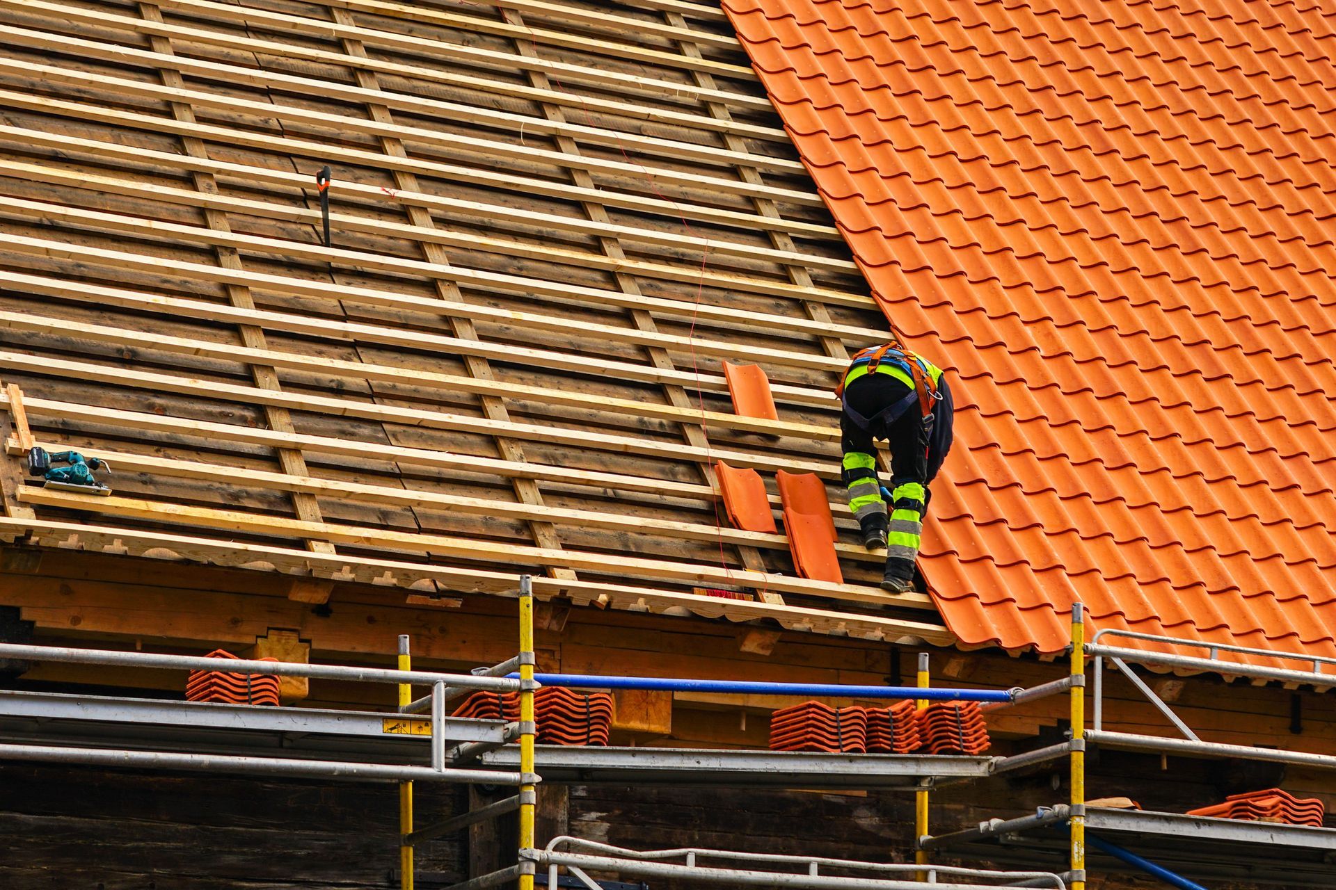 A male roofer in safety gear is installing new tiles during a roof replacement project. A male roofer in safety gear is installing new tiles during a roof replacement project.