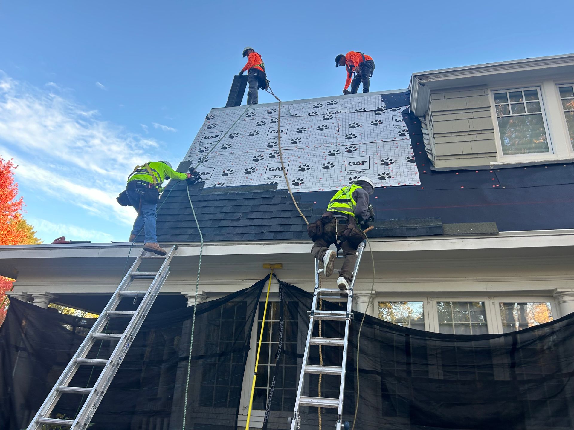 Four men performing roof repairs on a house, using tools and safety gear for maintenance work.