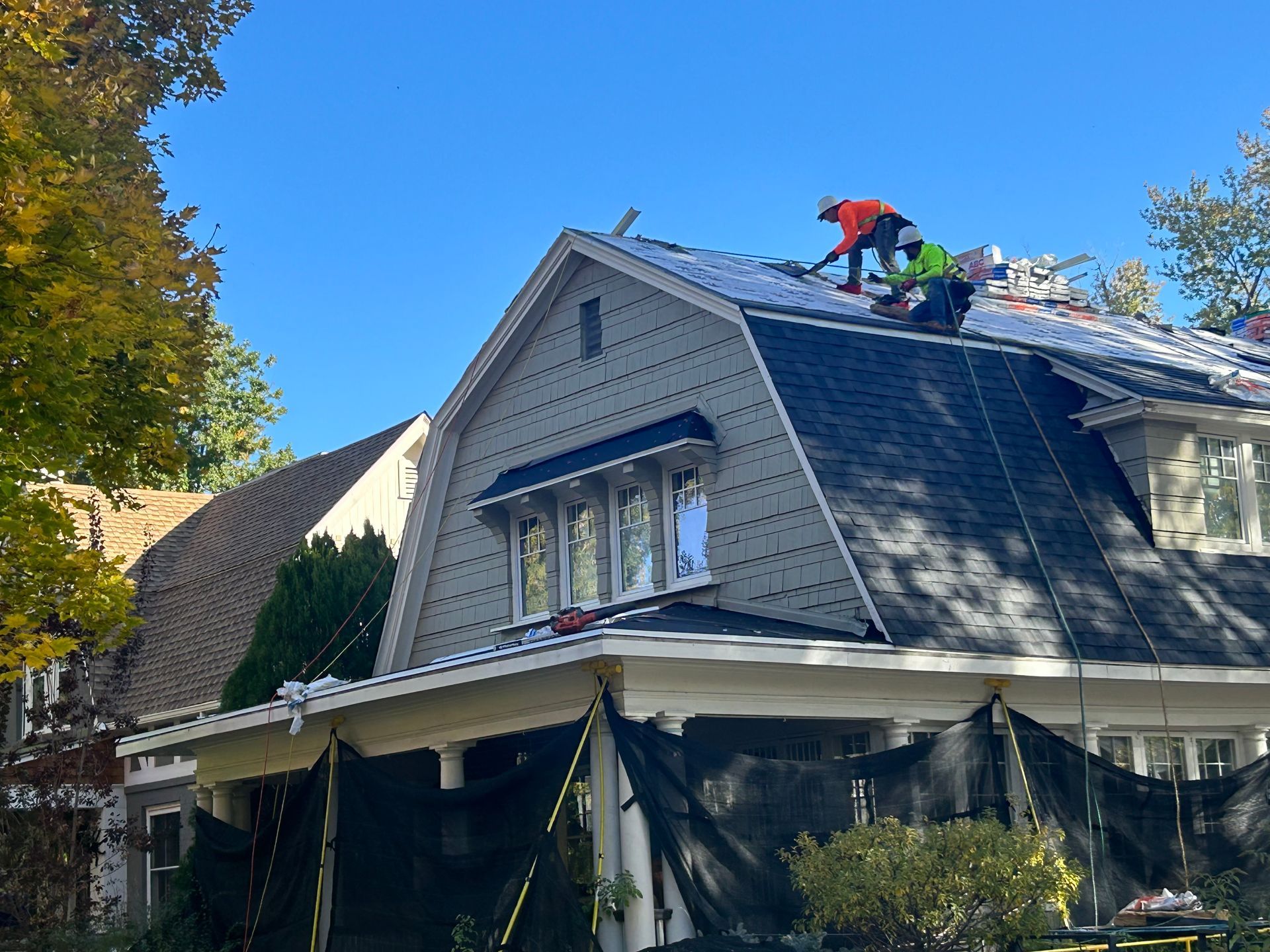 Two men performing roof repairs on a house, using tools and safety gear for maintenance work. Two men performing roof repairs on a house, using tools and safety gear for maintenance work.