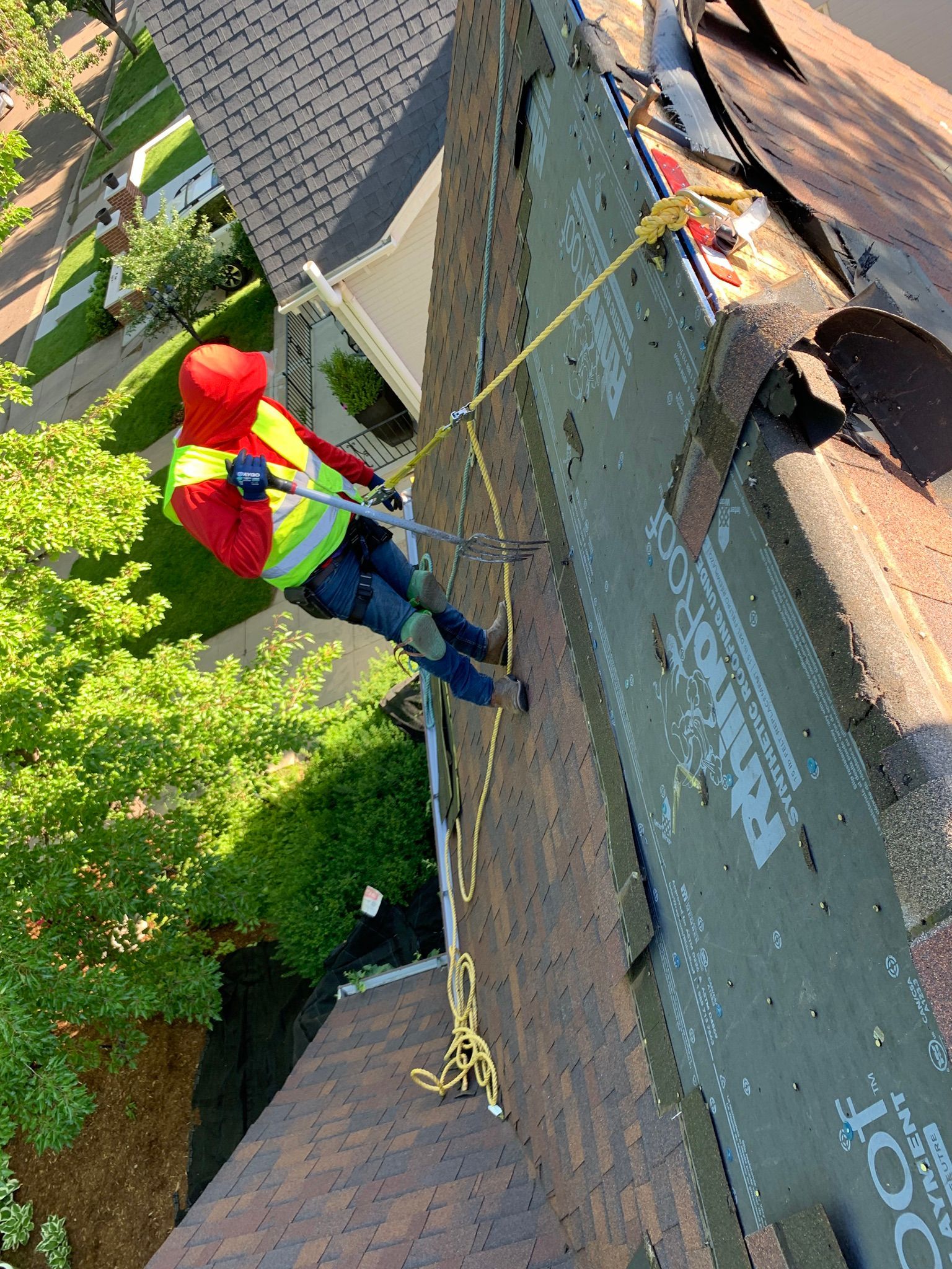 Worker in red helmet rappelling down a brick wall with ropes beside a building.