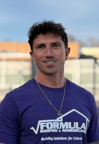 Man in purple shirt with logo, smiling outdoors.