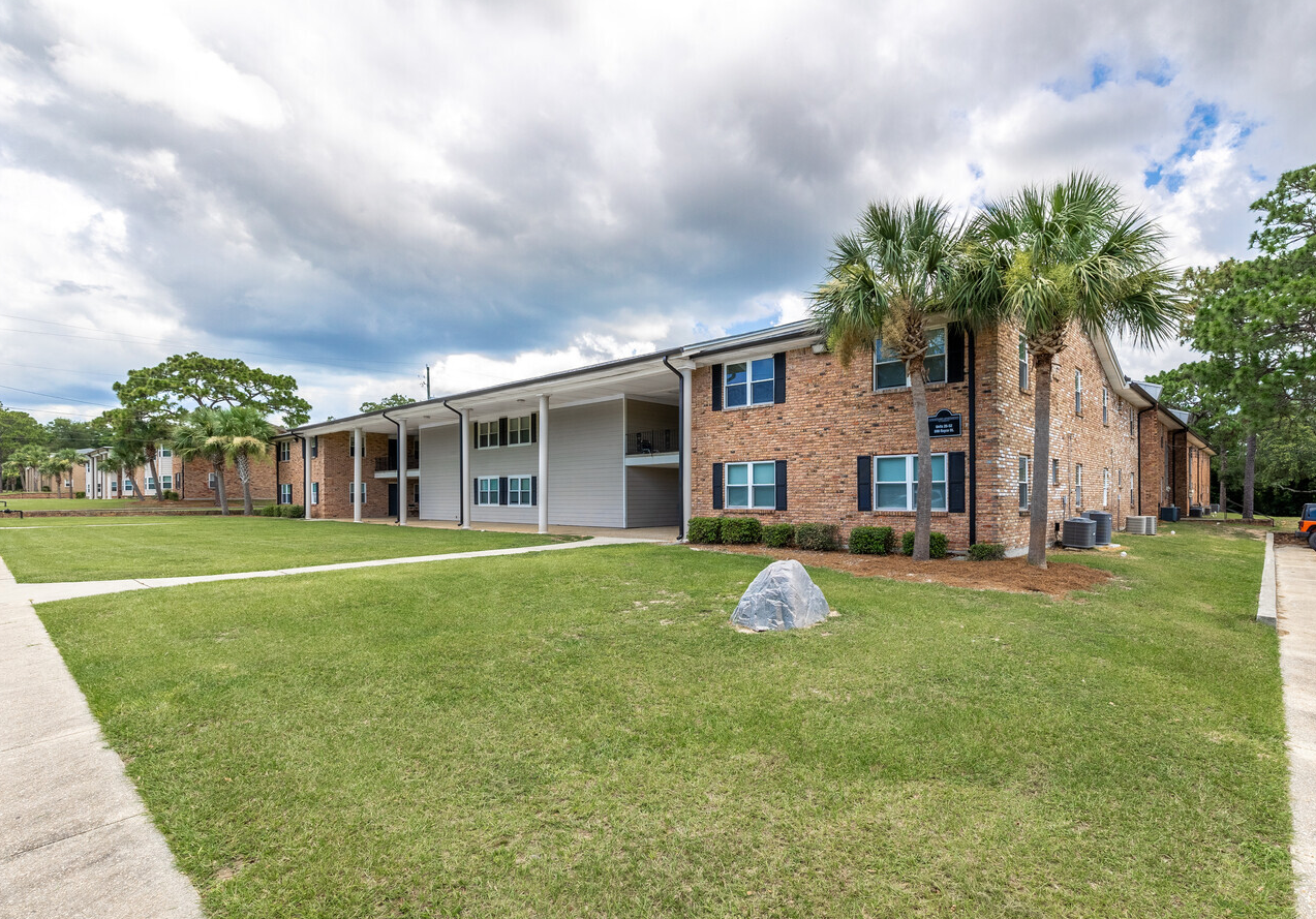 A large brick apartment building with a lush green lawn in front of it.