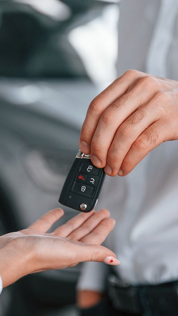 Person handing car keys to another person, blurred car in the background.