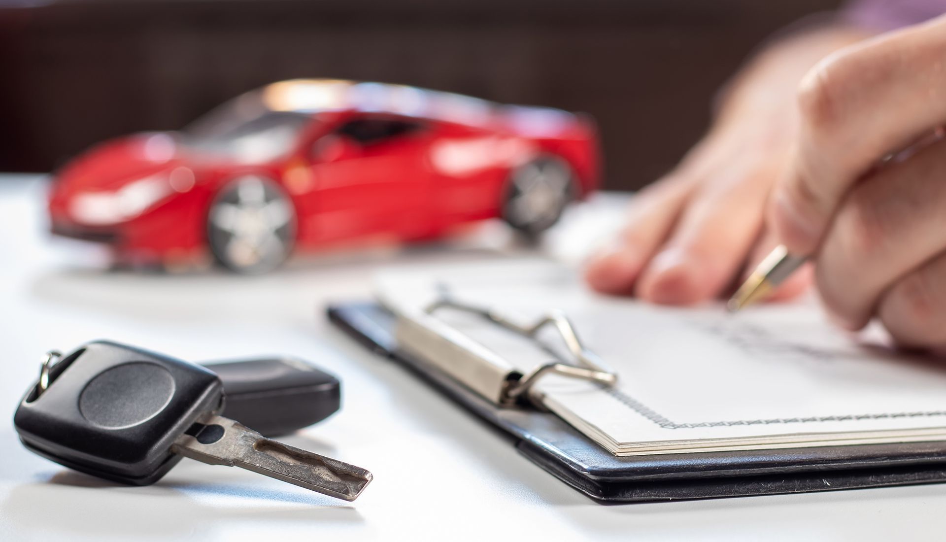 Car keys and a clipboard with a hand writing next to a red toy car.