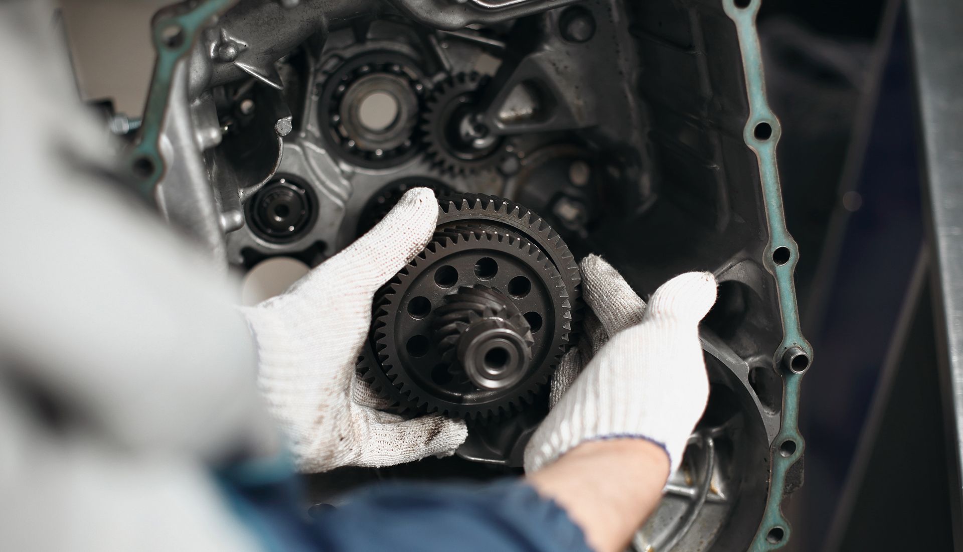 A person wearing gloves working on the gears inside a transmission, likely in a repair shop.