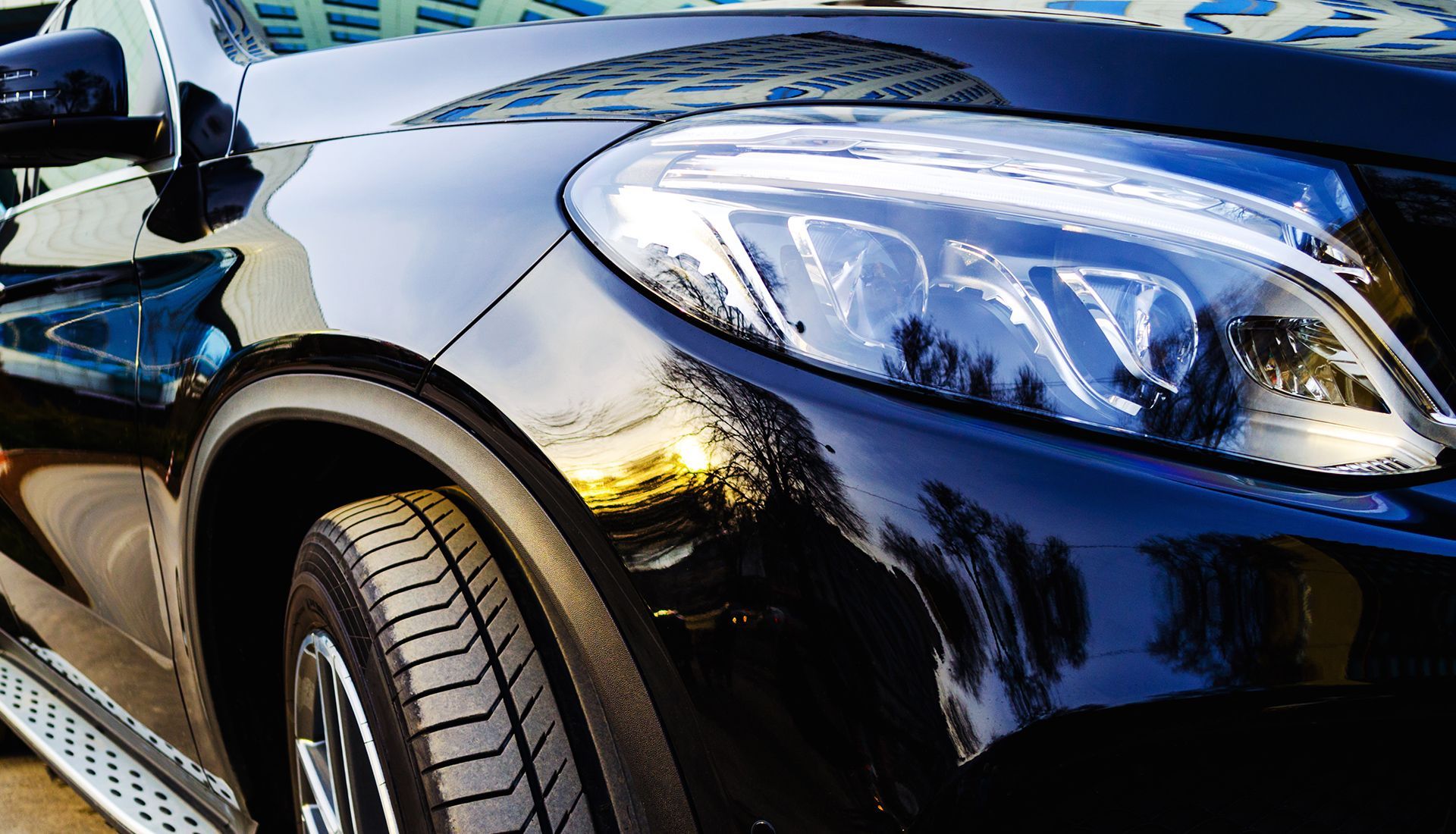 Close-up of a shiny black car's front quarter panel, tire, and headlight.