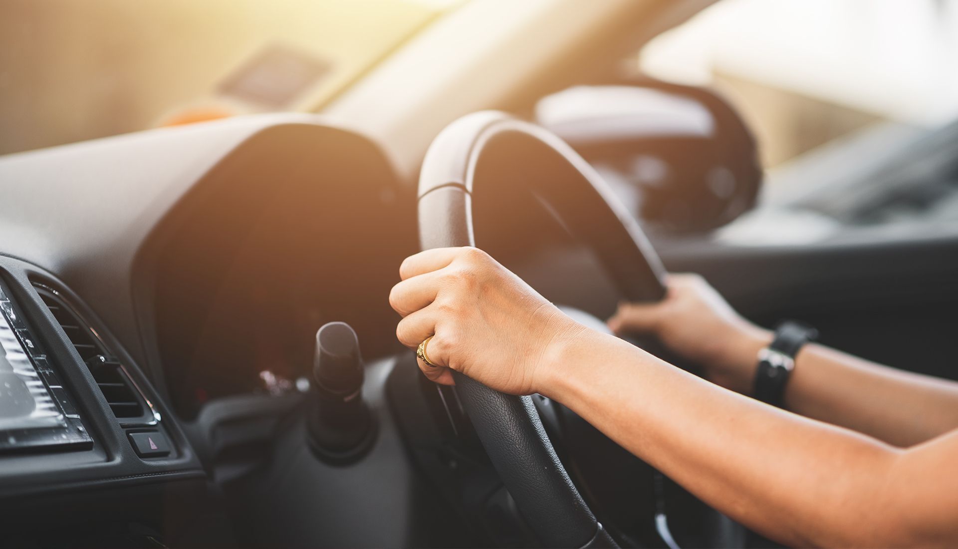 Hands gripping a black steering wheel inside a car, with a side mirror visible in the background.