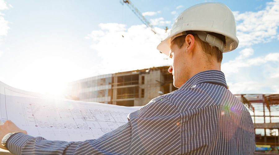 A man wearing a hard hat is looking at a blueprint at a construction site.