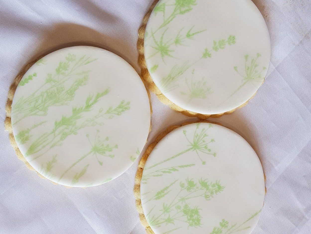 Three cookies with green flowers on them are sitting on a white cloth.