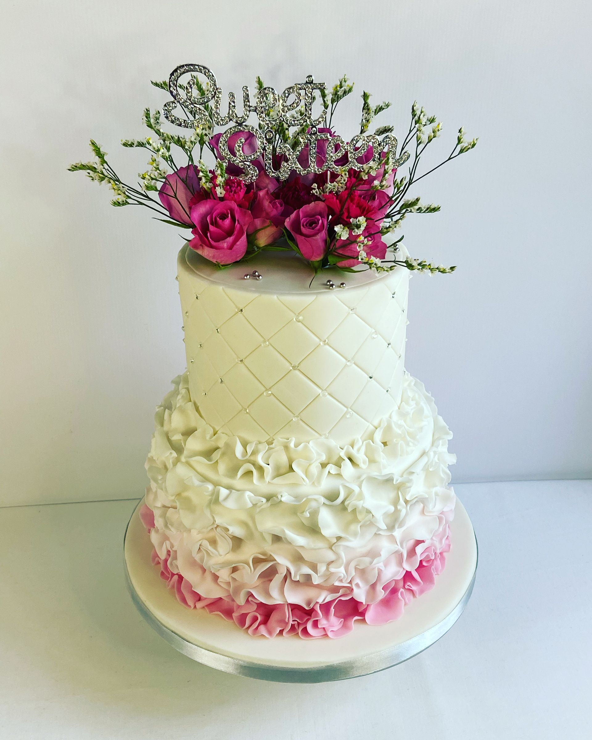 A white cake with pink ruffles and flowers on top