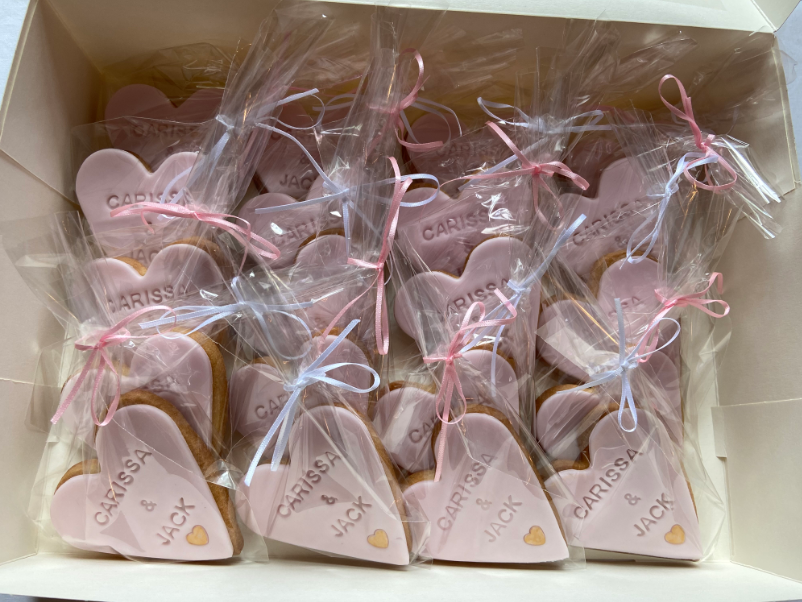 A box filled with pink heart shaped cookies with names on them.