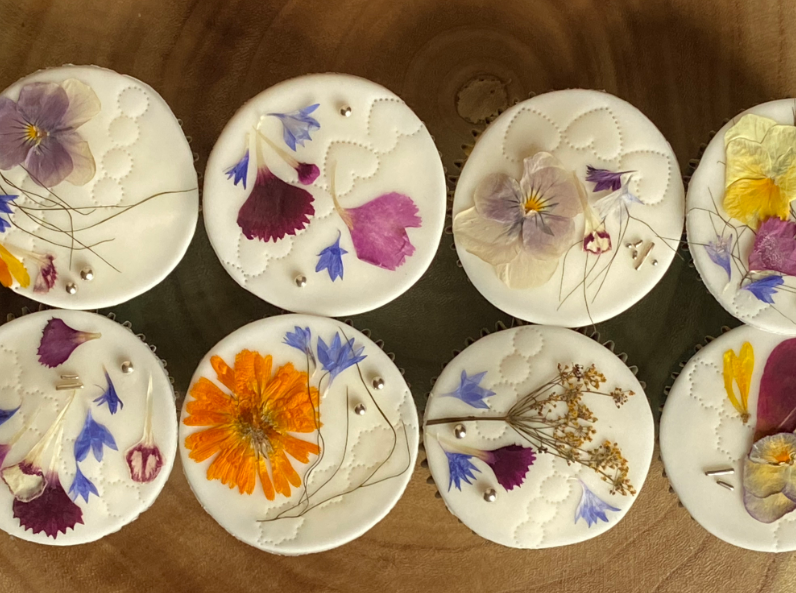 A row of cupcakes with flowers on them are sitting on a wooden table.
