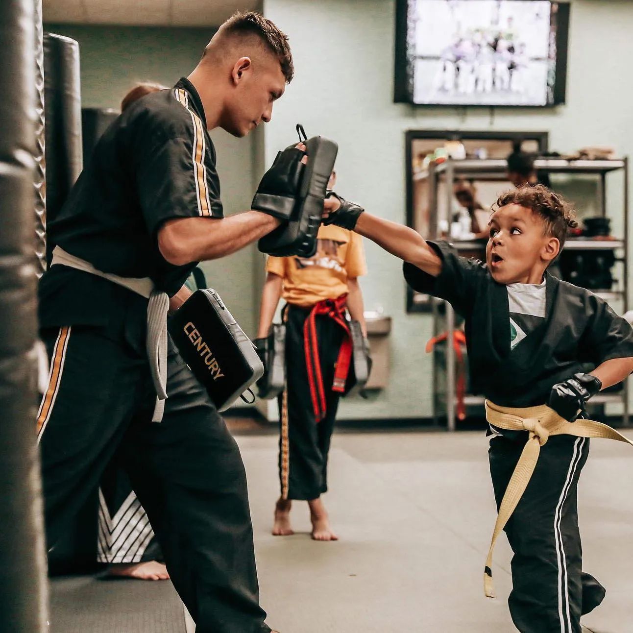 A man and a boy are practicing martial arts in a gym.