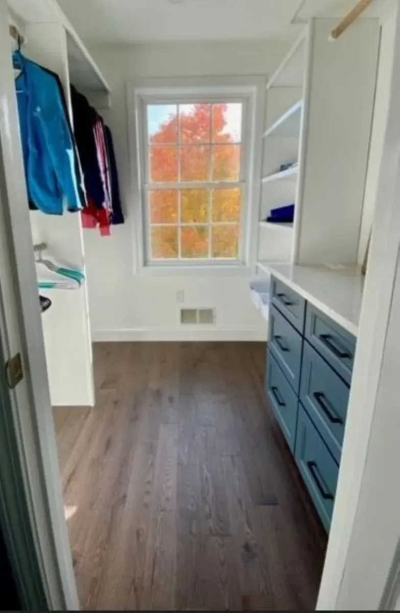 A walk in closet with a window and clothes on shelves