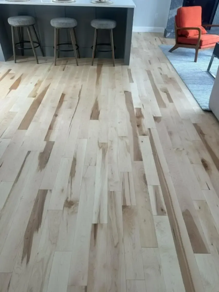 Light-colored hardwood floor in a room with a kitchen island and stools. An orange chair is in the background.