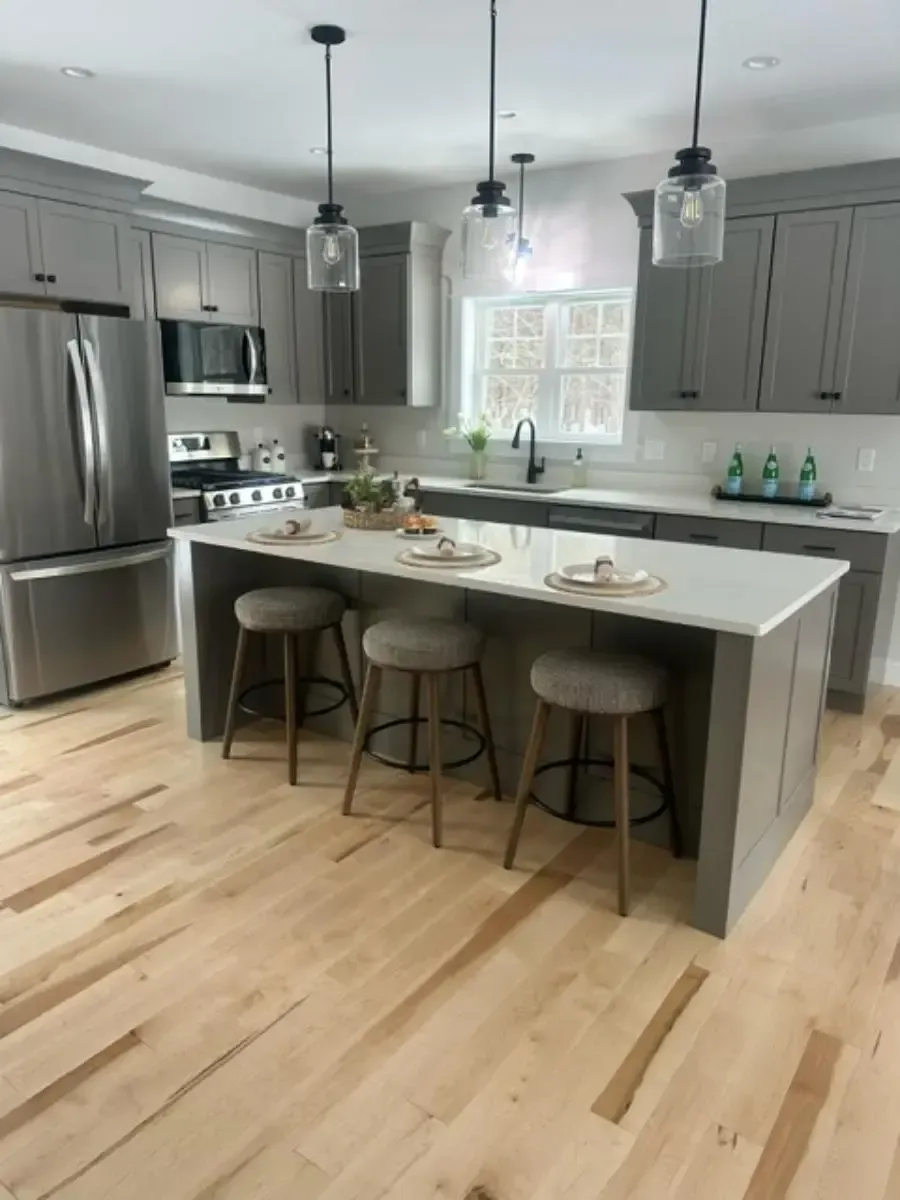 Gray kitchen with island, stools, stainless steel appliances, and pendant lights over the countertop.