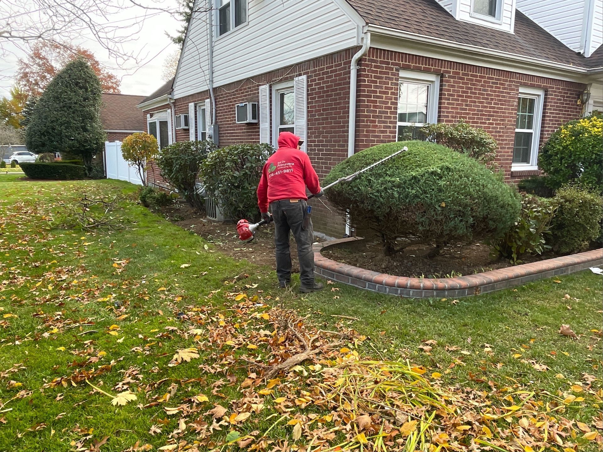 A man is cutting a bush in front of a house with a lawn mower.