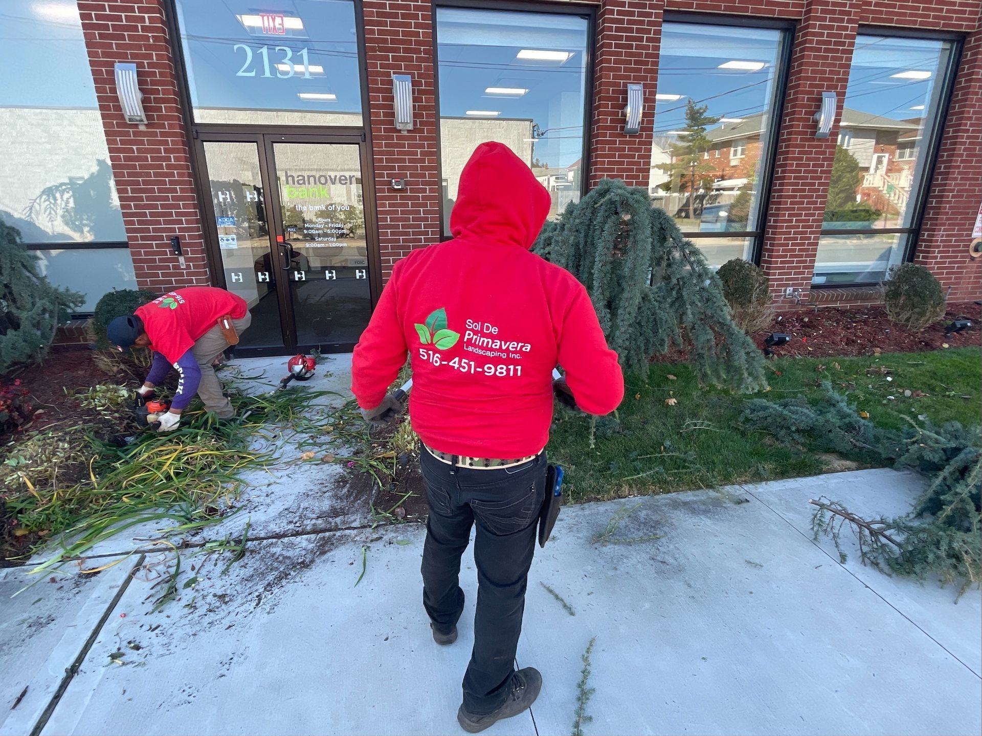 A man in a red hoodie is standing in front of a building.