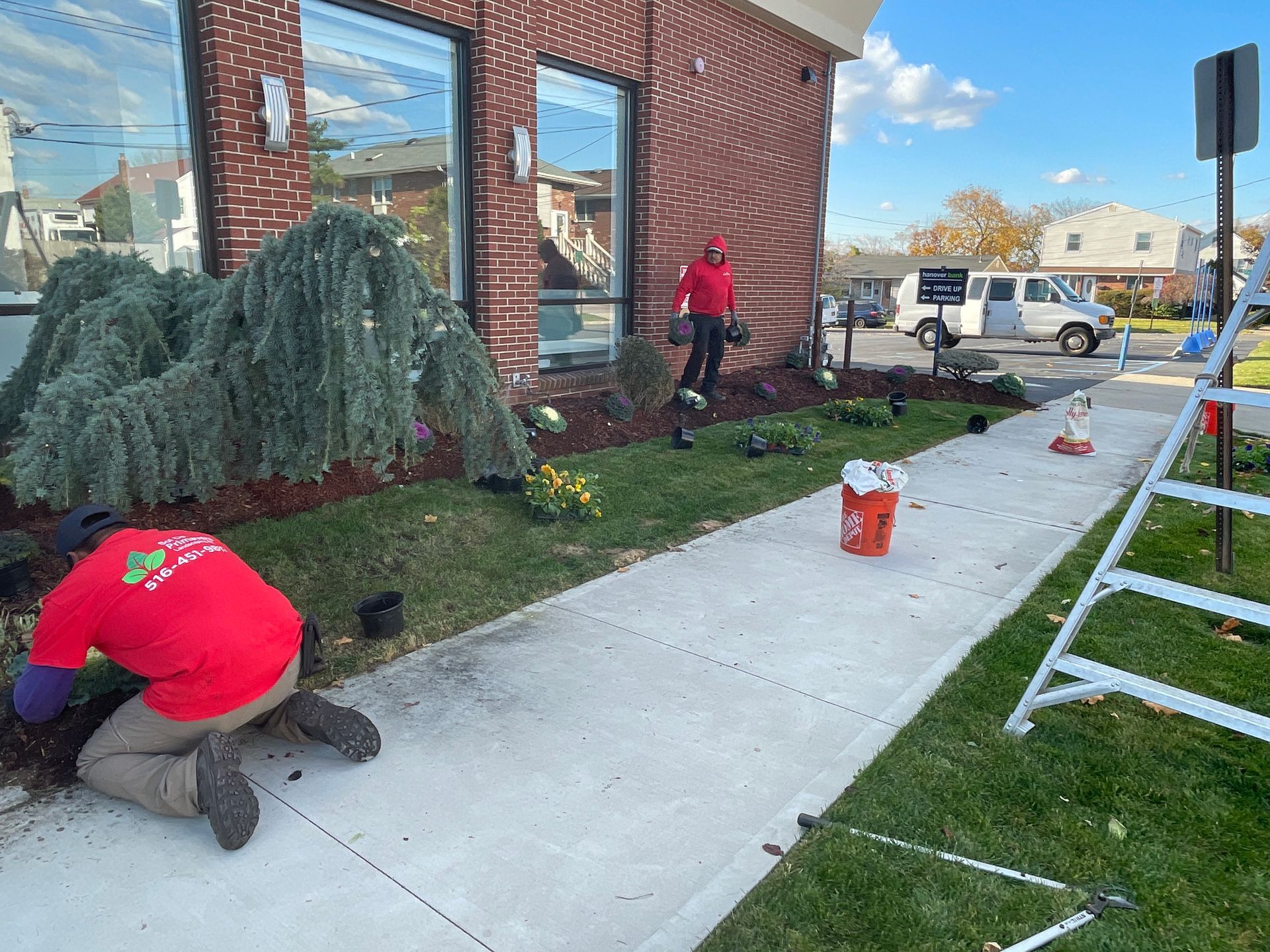 A man in a red shirt is kneeling on the sidewalk in front of a building.