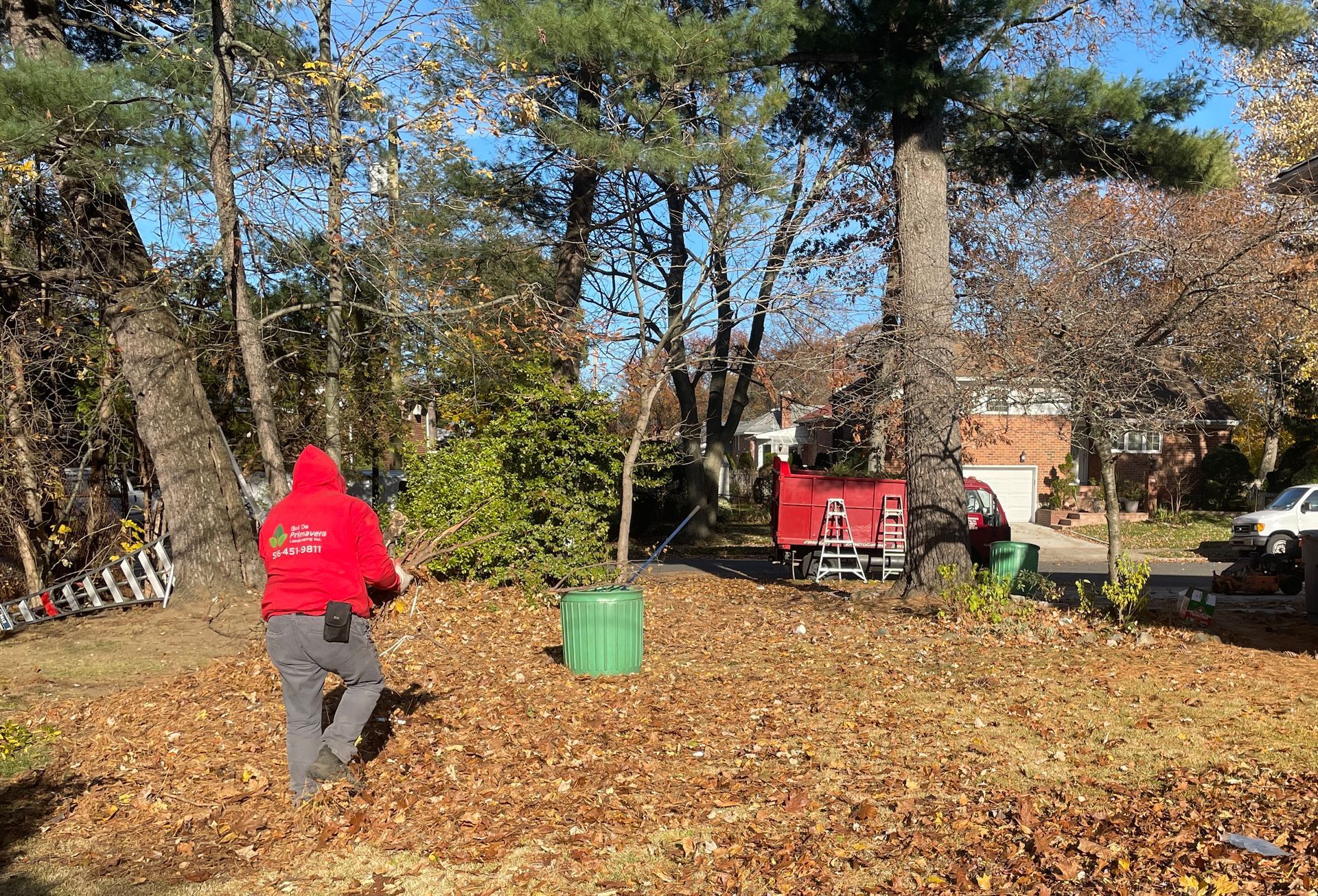 A man in a red jacket is raking leaves in a yard.