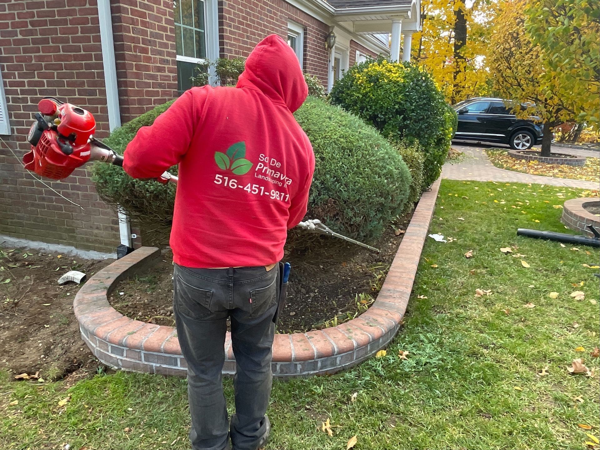 A man in a red hoodie is standing in front of a house holding a lawn mower.