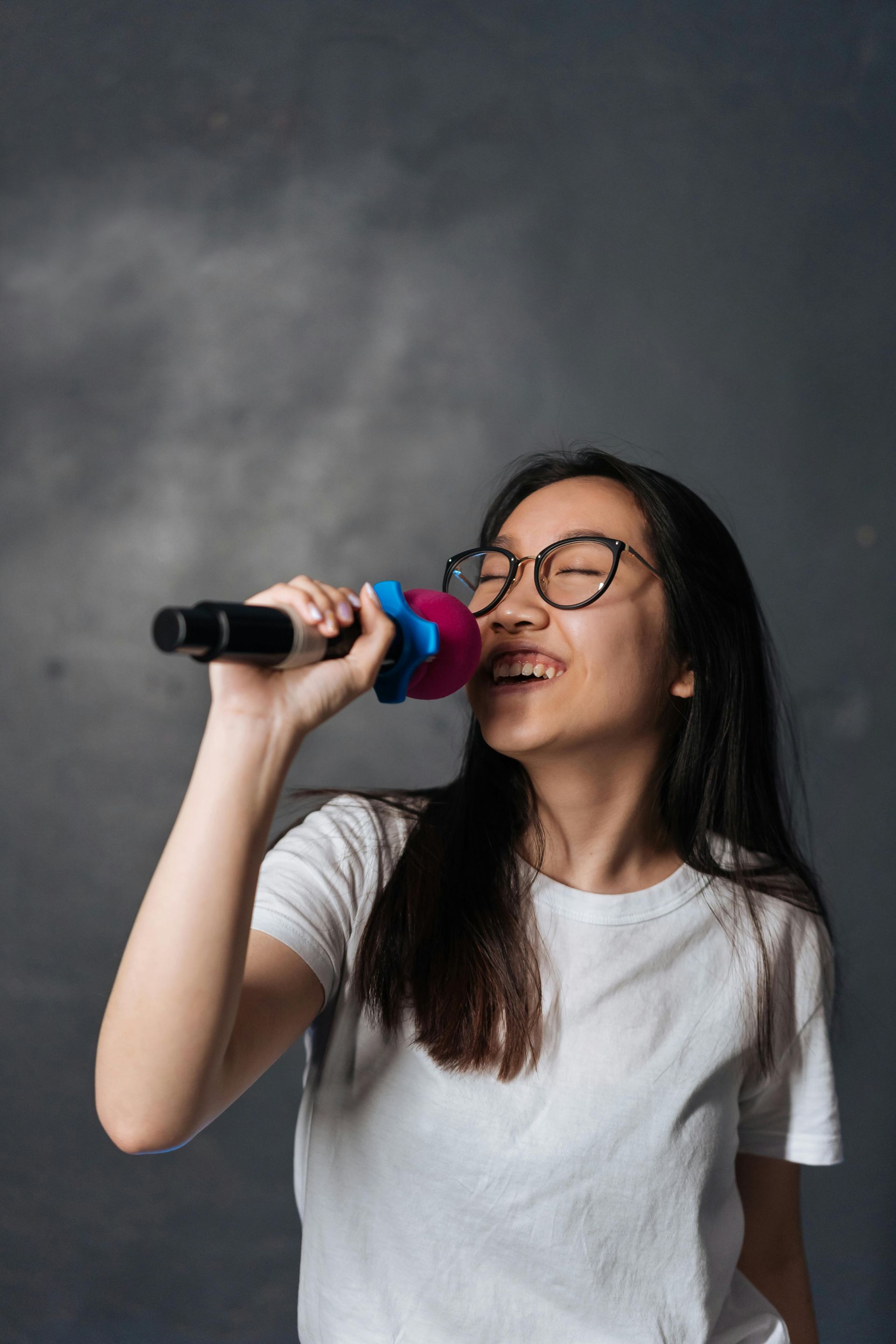 A woman wearing glasses is singing into a microphone.