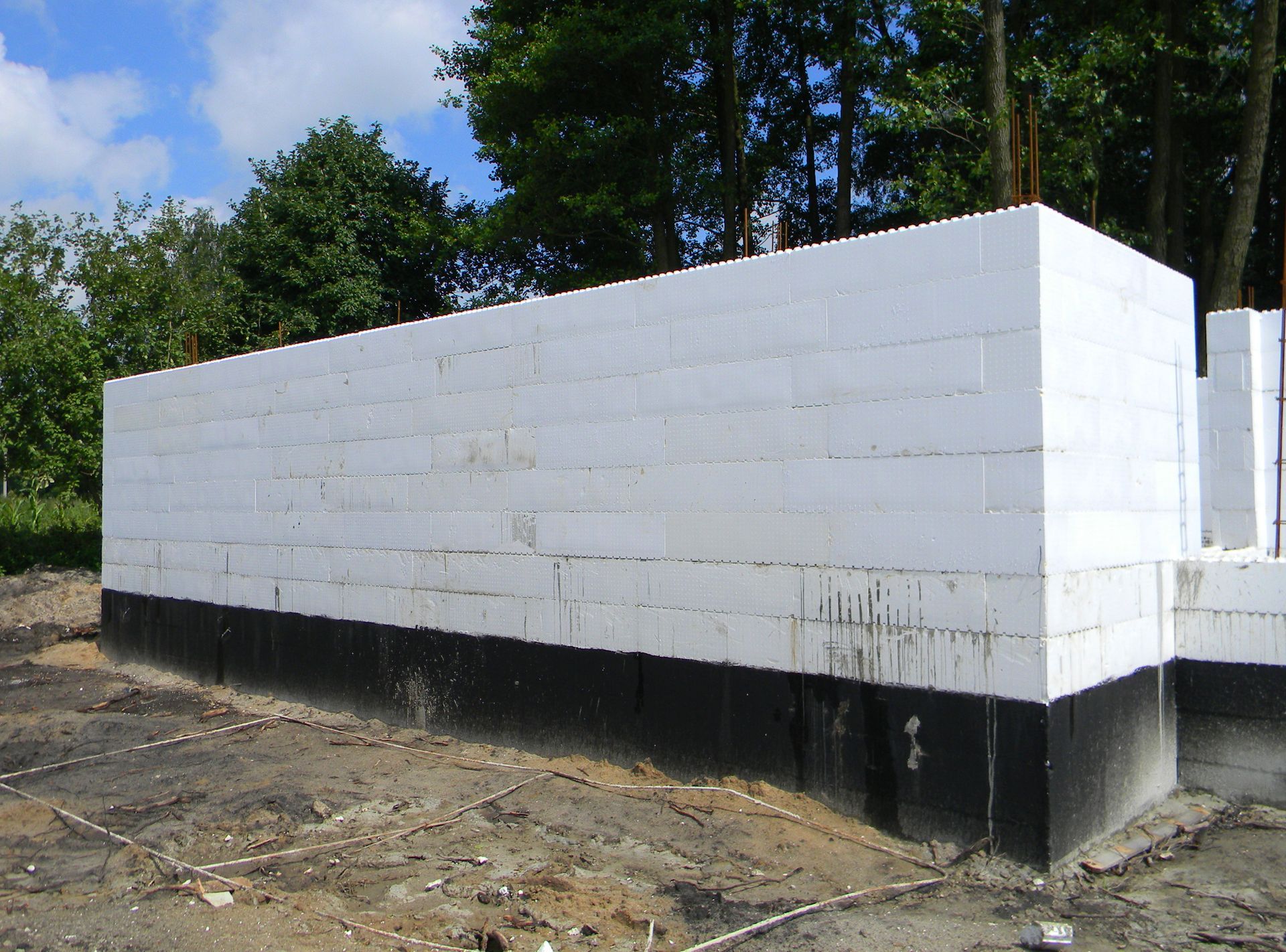 Partially built white cinder block foundation on a dirt lot with trees in the background
