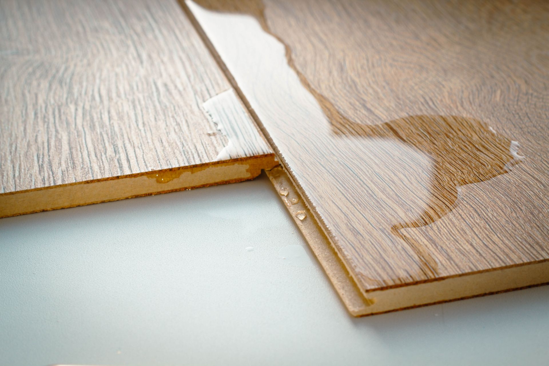 Water spill on light wooden flooring with visible wet patches and a seam between panels