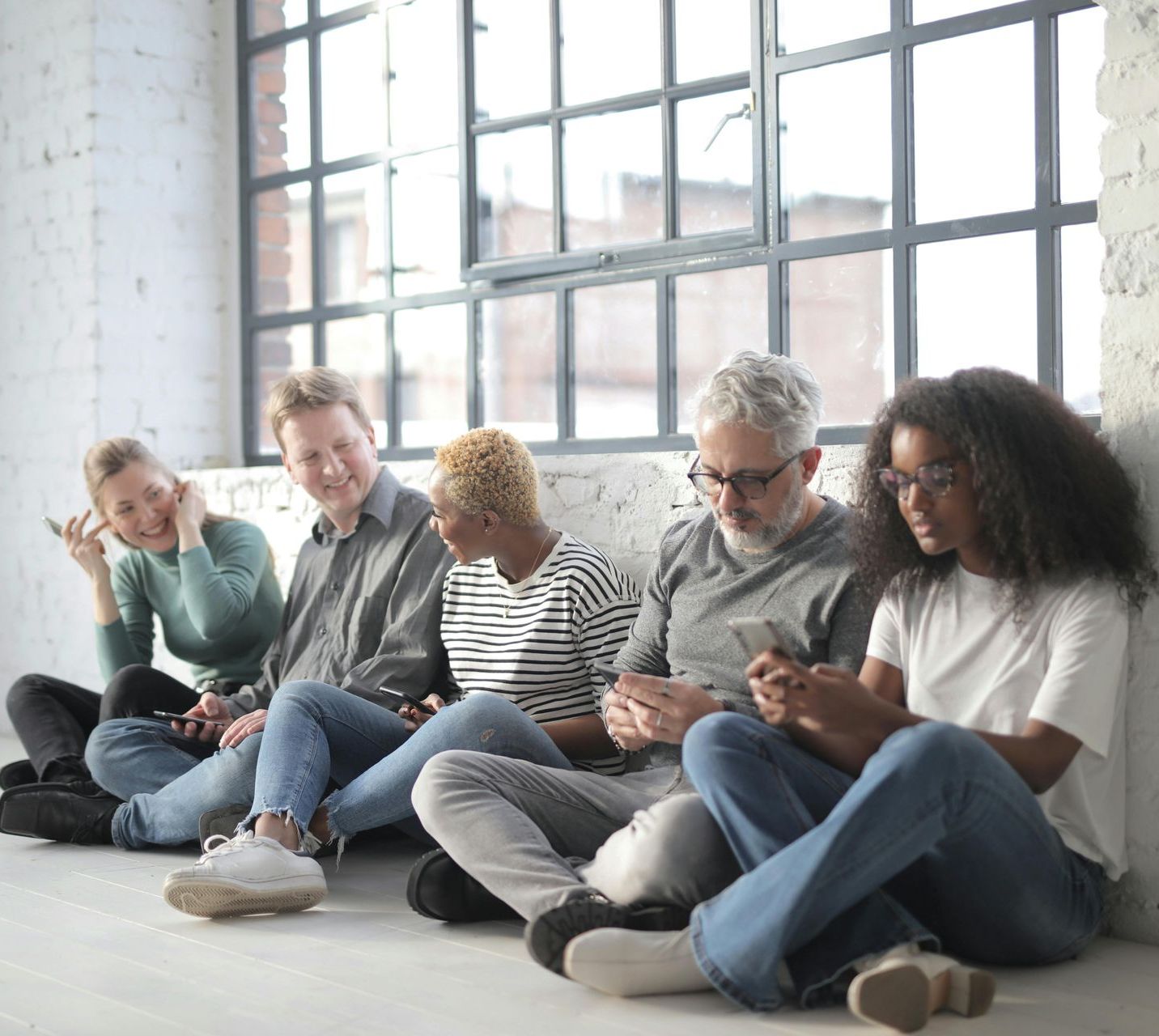 A group of people are sitting on the floor looking at their phones.