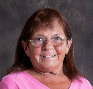 A woman wearing glasses and a pink shirt is smiling for the camera.