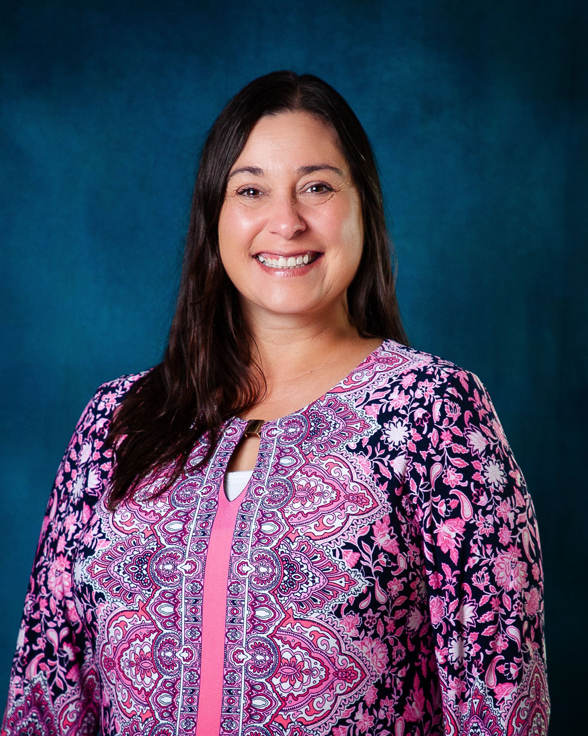 A woman in a pink and blue shirt smiles for the camera