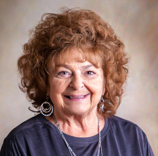 A woman with curly hair wearing a necklace and earrings smiles for the camera