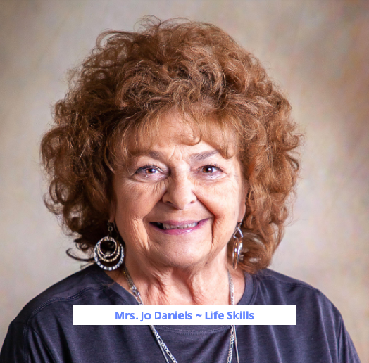 A woman with curly hair wearing a necklace and earrings smiles for the camera