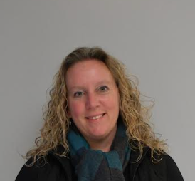 A woman wearing a black jacket and a blue scarf is smiling for the camera.