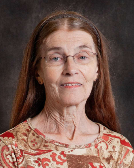 A woman wearing glasses and a headband smiles for the camera