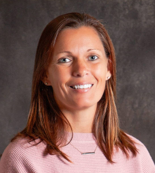 A woman wearing a pink sweater and a necklace is smiling for the camera.