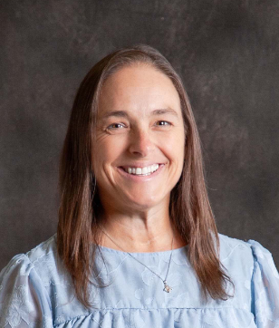 A woman wearing a blue shirt and a necklace is smiling for the camera.