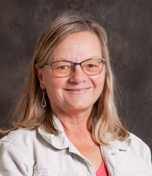 A woman wearing glasses and a white jacket smiles for the camera