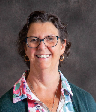 A woman wearing glasses and a floral shirt is smiling