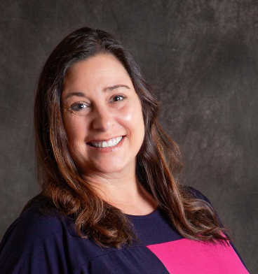 A woman in a pink and blue shirt smiles for the camera